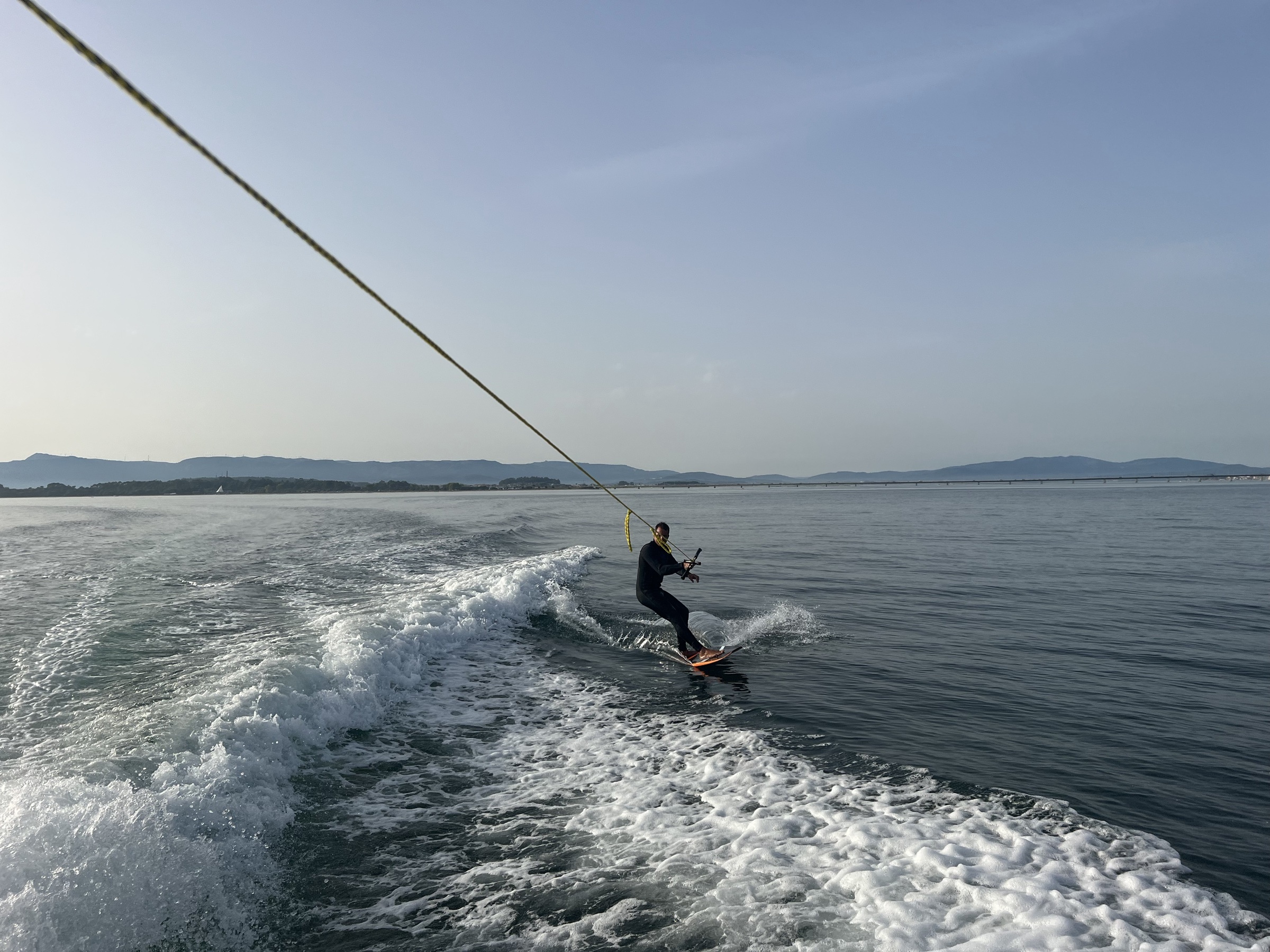 Wakeboarder cruzando la estela del barco con horizonte de bateas al fondo en las Rías Baixas