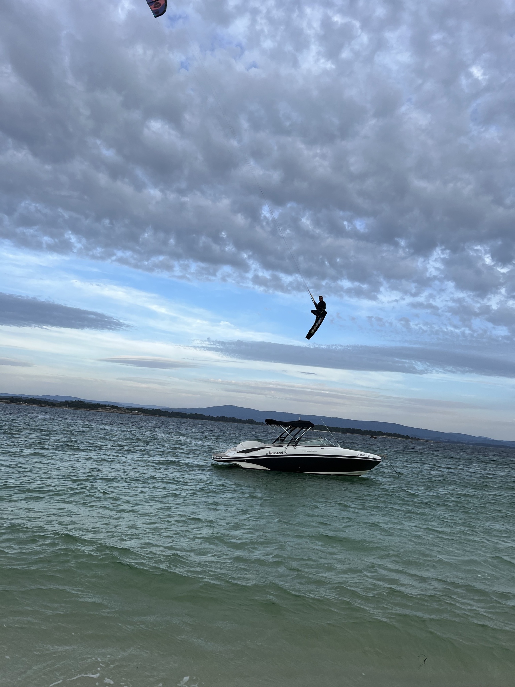 Kitesurfer saltando con la cometa al viento sobre las aguas de las Rías Baixas con el barco como base flotante